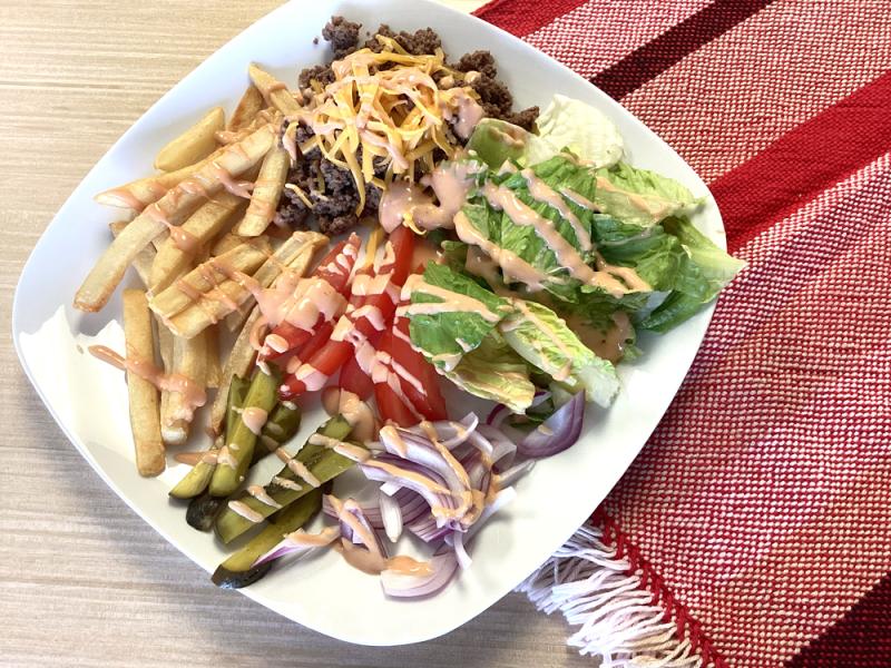 white plate with burger bowl components on top and drizzled with sauce