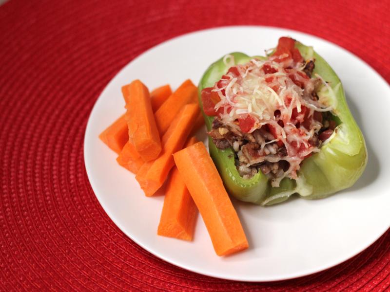 green pepper stuffed with venison, tomatoes, topped with cheese on a white plate