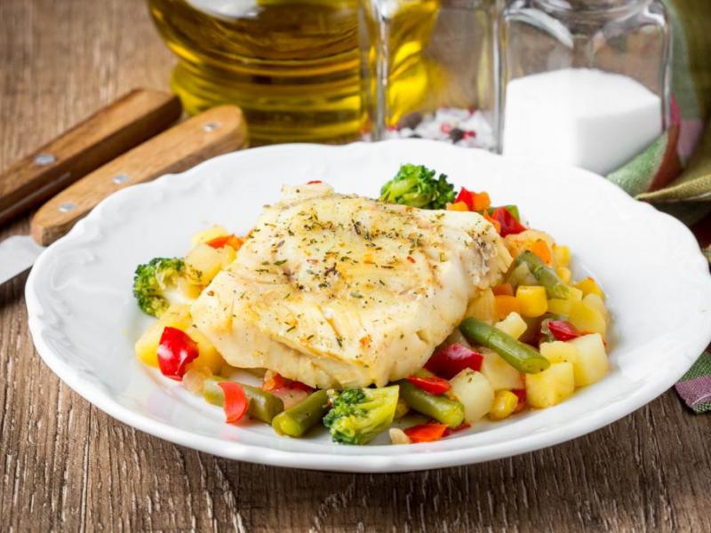 Seasoned Baked Fish atop mixed vegetables on a white plate