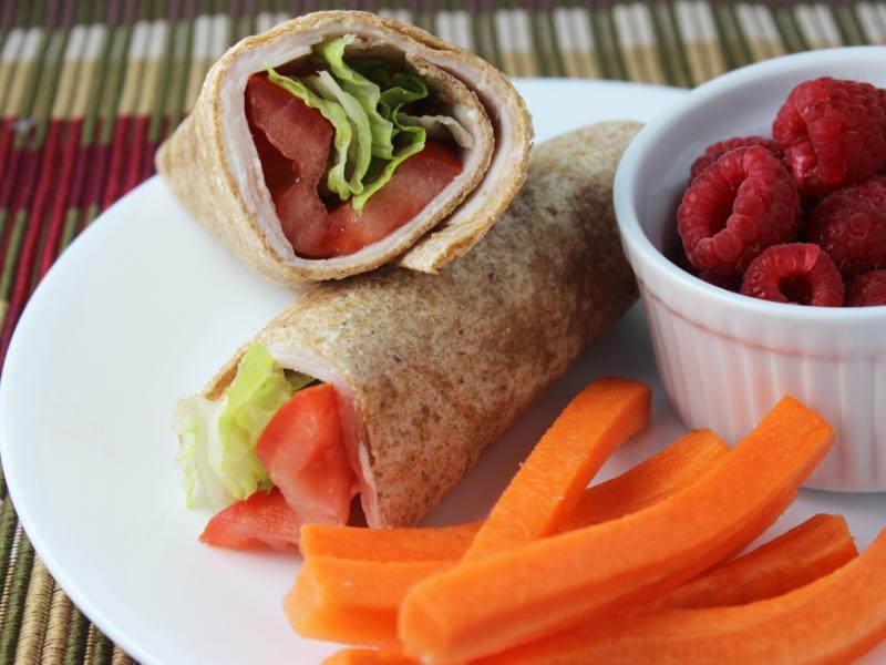 Turkey Sandwich Wraps served on a white plate with dish of raspberries and side of carrot sticks