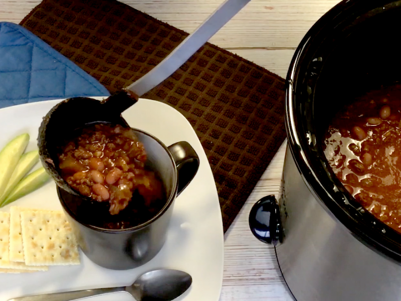 venison chili being ladeled from a slow cooker into a cup with side of saltine crackers