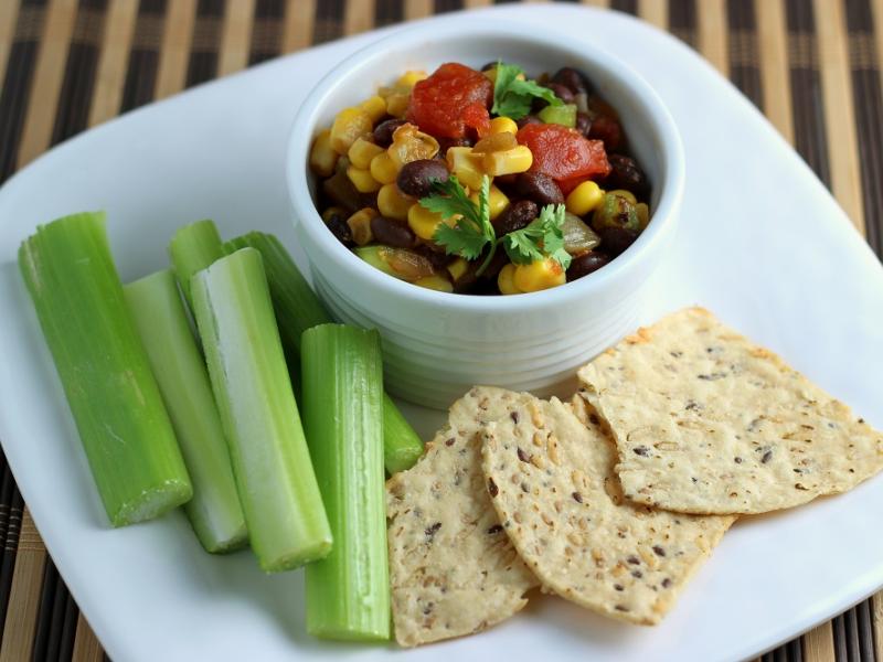 Confetti Bean Salsa in a white dish served with whole grain chips and celery sticks