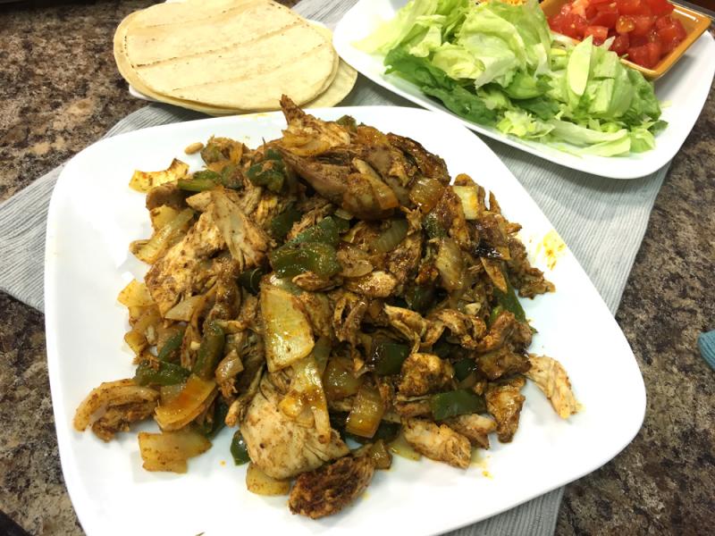 Chicken Fajitas on a white plate with side of tortillas, lettuce and diced tomatoes