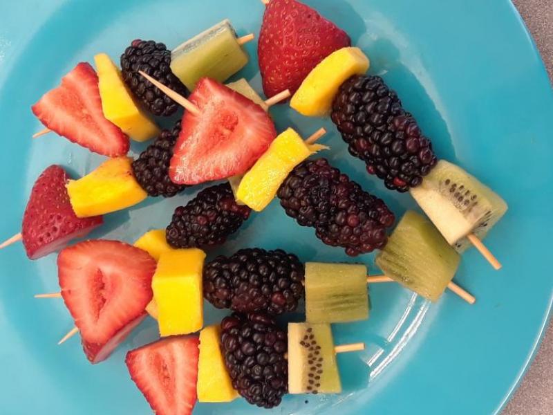 seven fruit kabobs on a blue plate