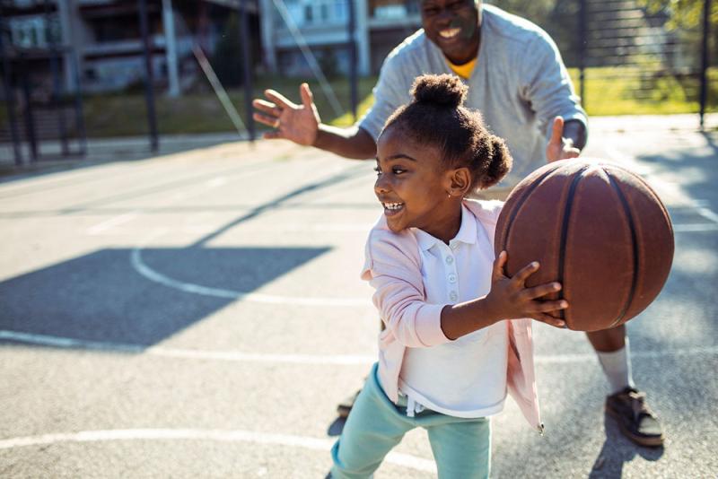 girl and grandfather playing basketball outside