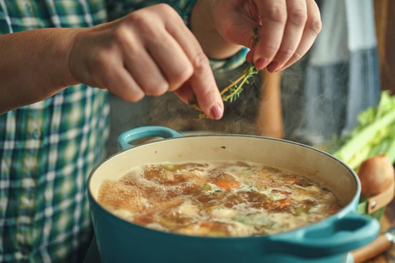 adding herbs to broth cooking in pot on stove